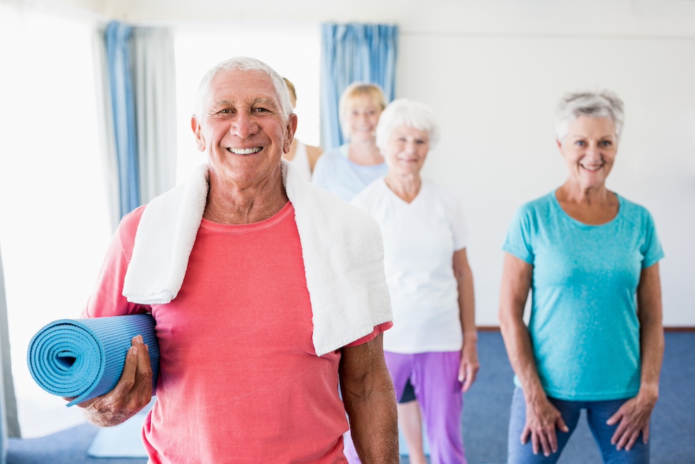 Senior man holding yoga mat during a group fitness class