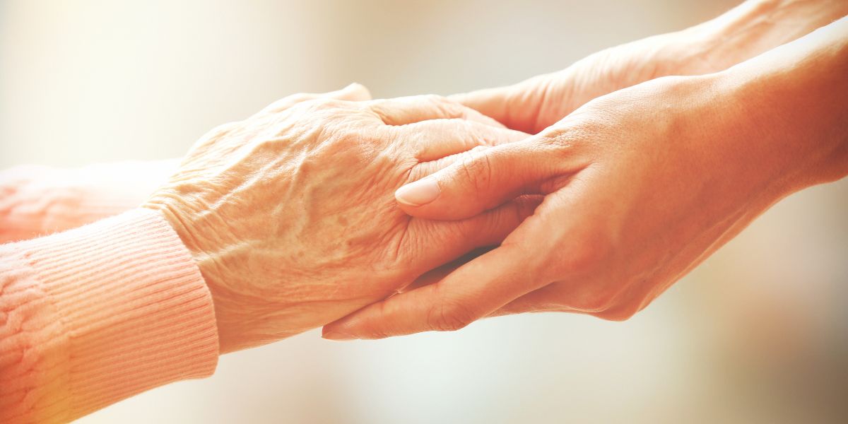 A close up of a senior woman holding hands with her caregiver